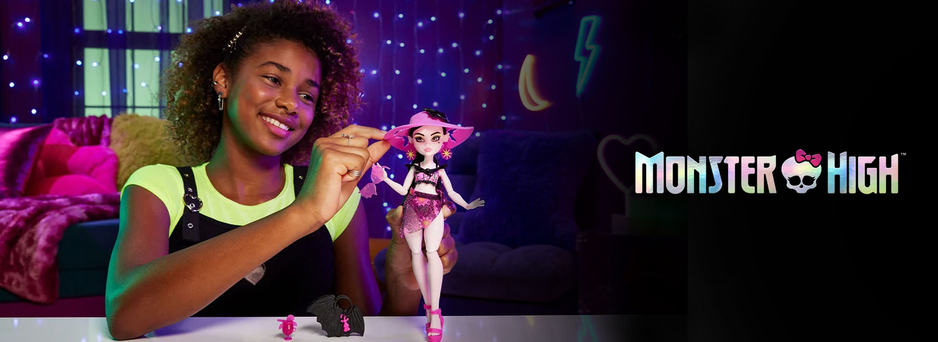 Pige leger med dukke i et lysdekoreret rum, Monster High-logo ses.
