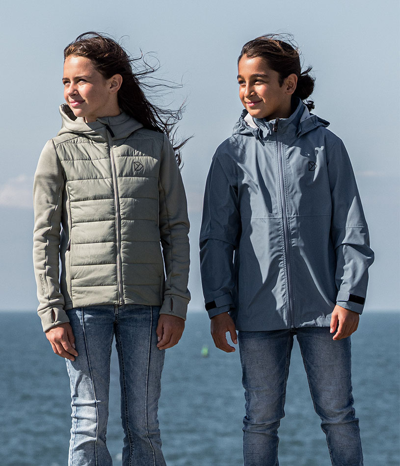 To børn i veste går på en grusvej ved kysten.