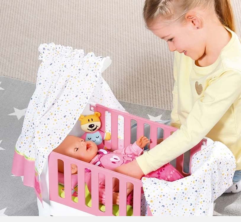 Pige leger med dukke i lyserød tremmeseng med legetøjsgardin og bamse.