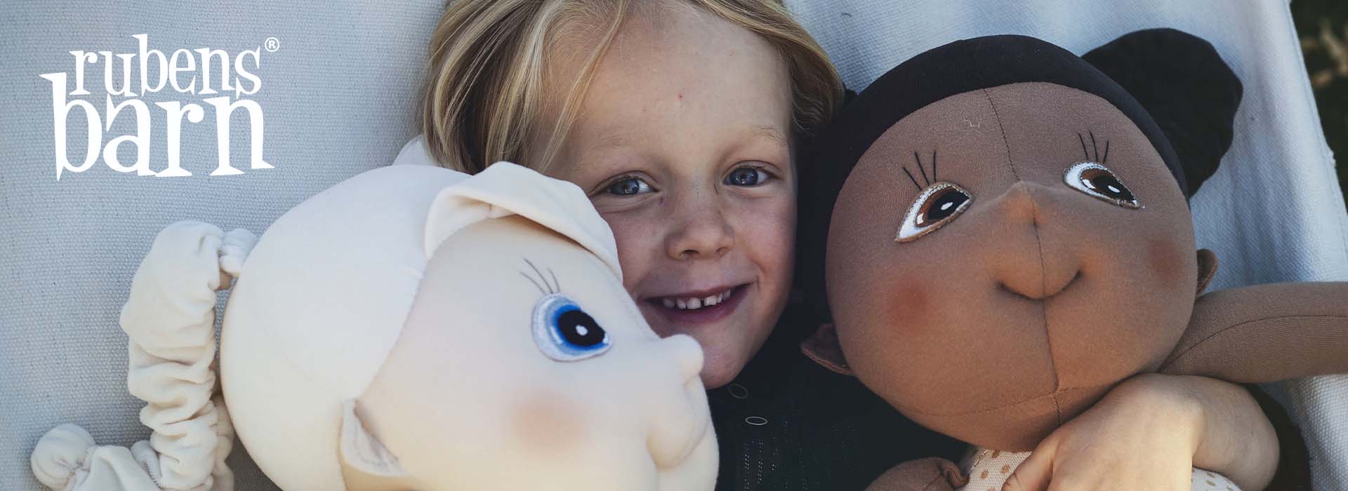 Barn med to dukker, smilende ansigt ved siden af bløde dukker.