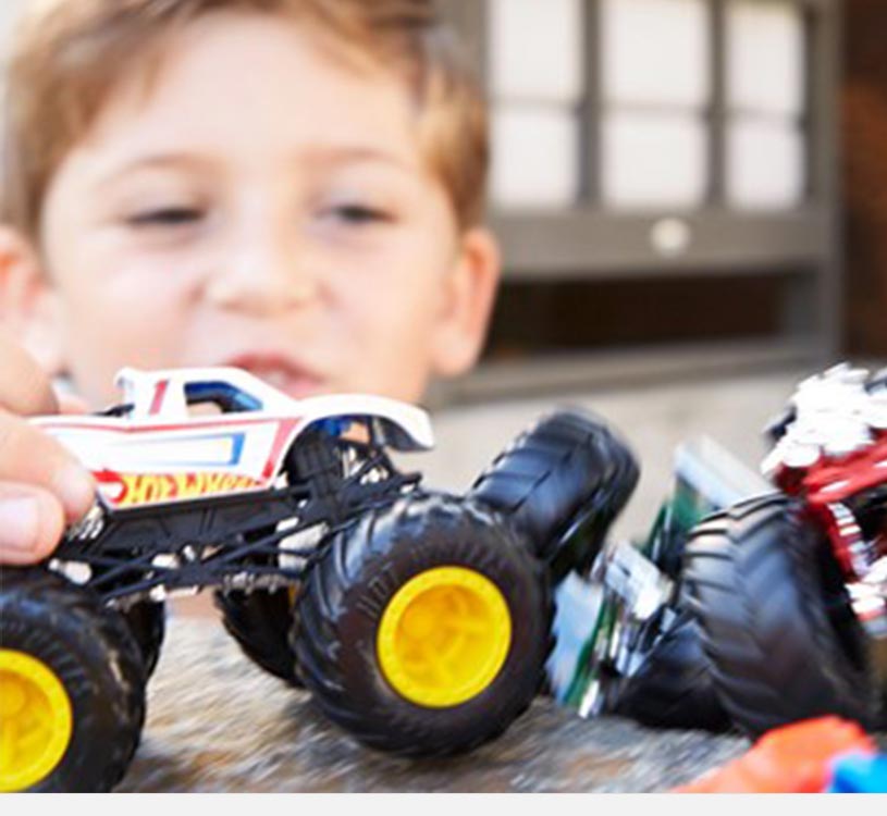 Dreng leger med monstertruck-legetøjsbiler på et bord.
