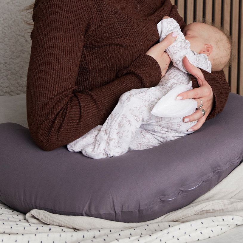 Person ammer baby med støtte fra pude, brun trøje.