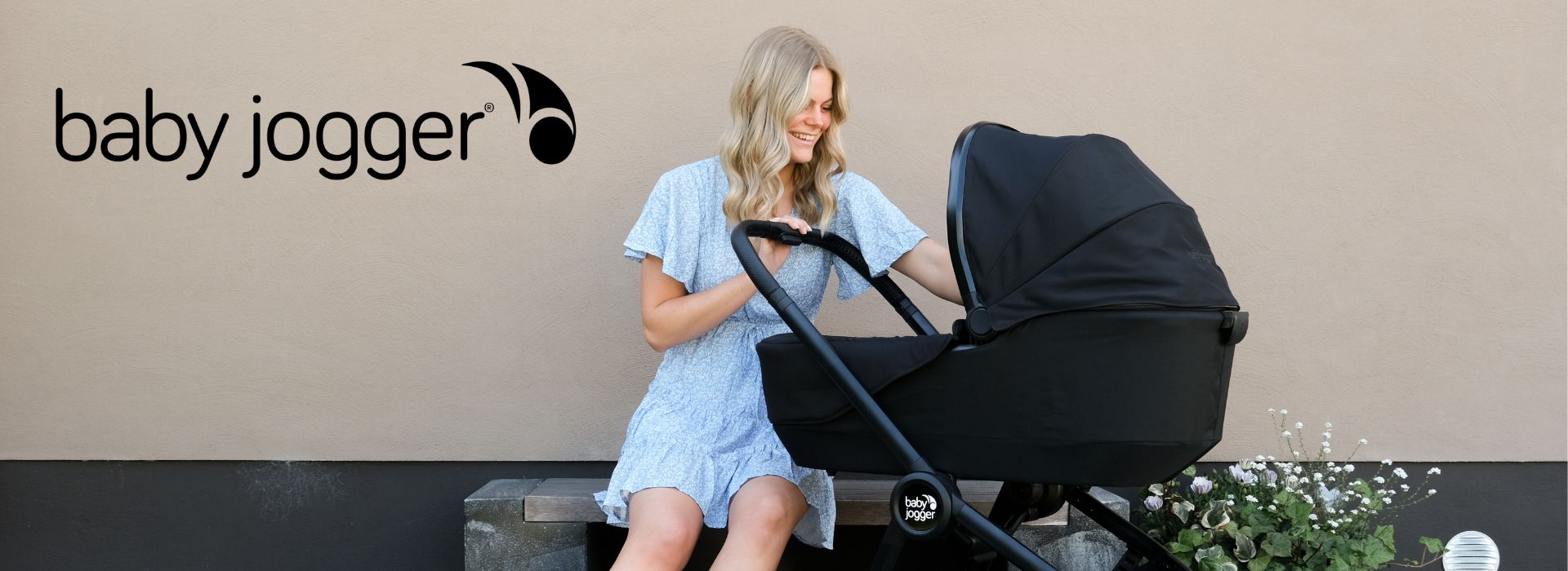 Kvinde i blå kjole sidder ved siden af en sort barnevogn fra Baby Jogger.