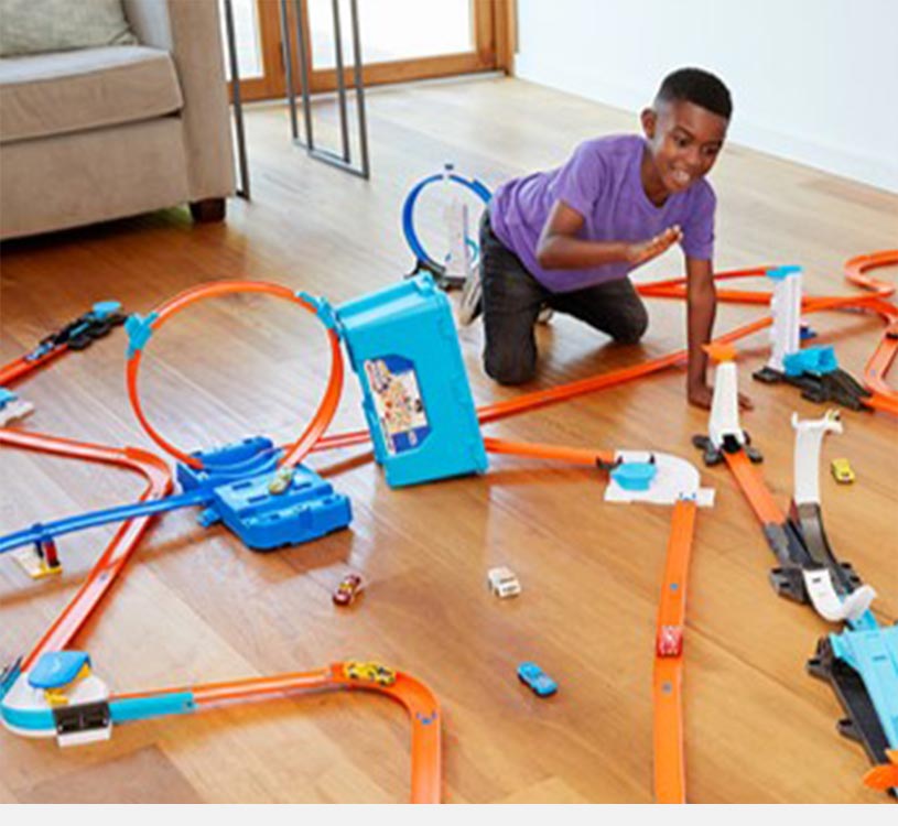 Barn leger med et bilbanesæt og farverige biler på trægulv.