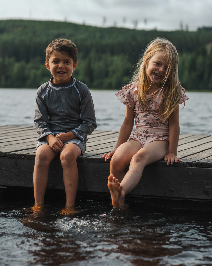 To børn sidder på en bro med fødderne i vandet.