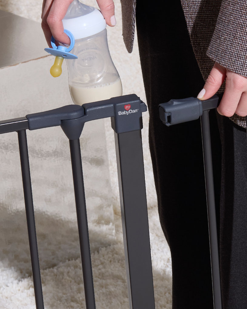 En person holder en sutteflaske ved en BabyDan skruvgrind.