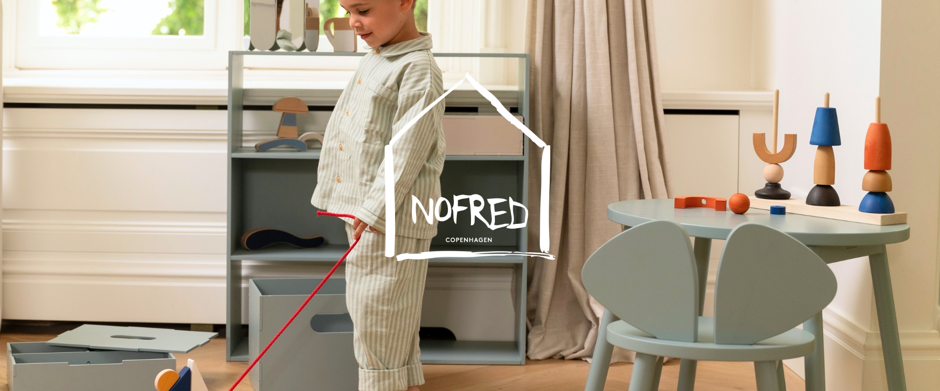 Barn i pyjamas leger med legetøj i et lyst rum.