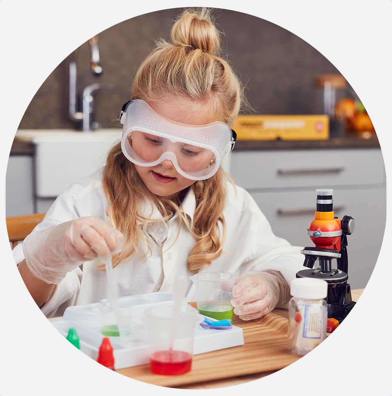 Barn i laboratoriekittel og beskyttelsesbriller eksperimenterer med væsker ved mikroskop.