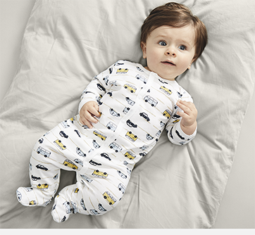 Baby i pyjamas med bilprint ligger på et gråt tæppe.