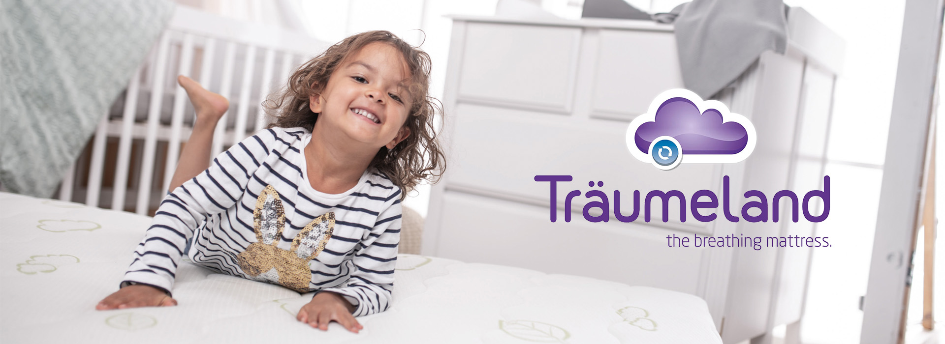 Barn ligger på hvid madras ved siden af Träumeland-logo.