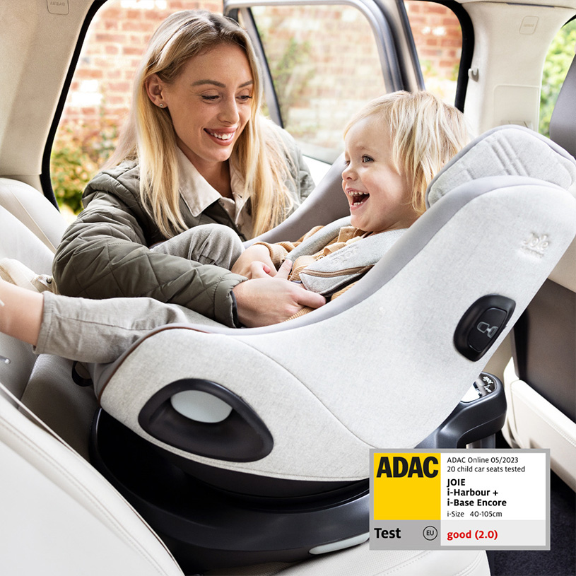 Kvinde smiler til barn i autostol i bil.