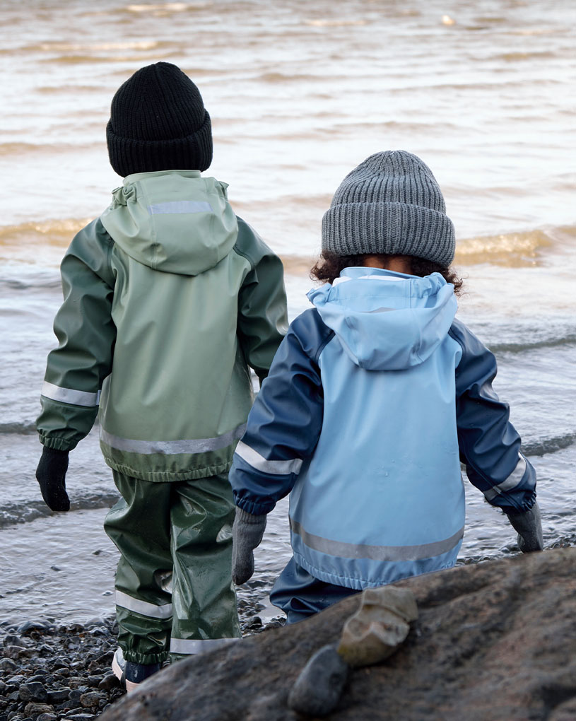 To børn i regntøj leger i vandet ved en strand.