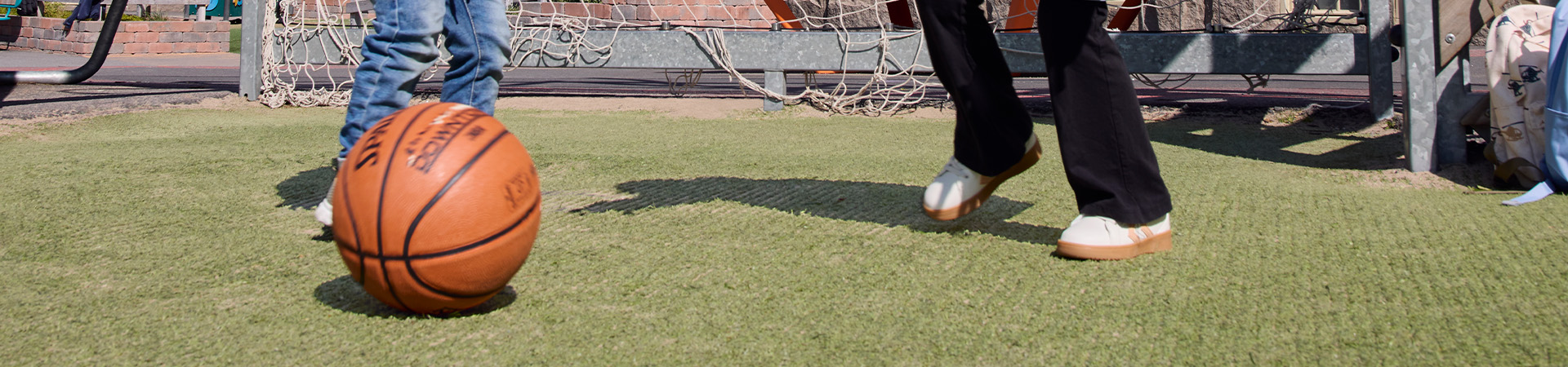 Børn spiller fodbold på græs foran et mål.