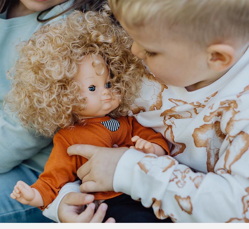Dreng holder en dukke med krøllet hår og orange tøj.
