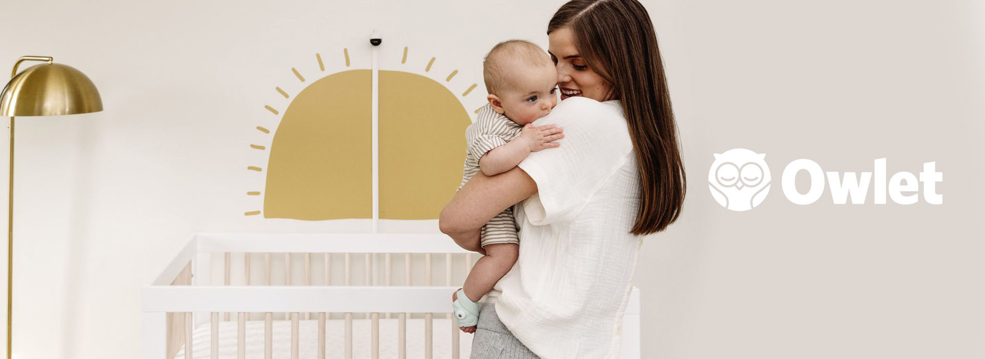 Kvinde holder en baby i et rum med pastelfarver og en sol vægmaleri.
