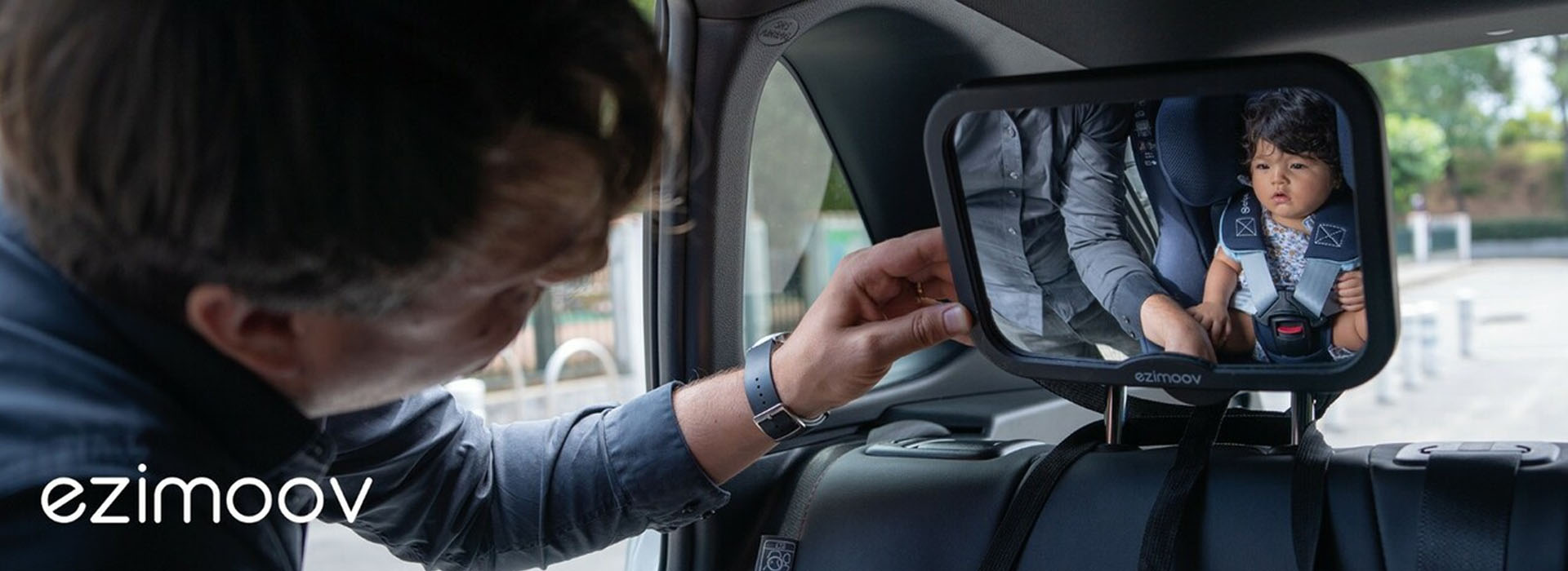 Mand justerer bilspejl for at se barn i autostol.