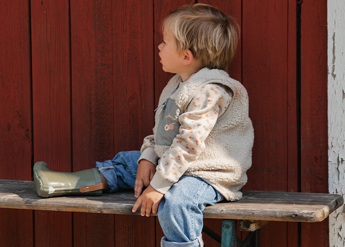 Barn sidder på en bænk iført en vest og gummistøvler, med teksten 'Kenza X Viking'.