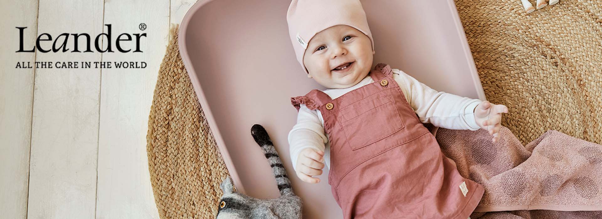 Smilende baby i rosa sele på rosa puslemåtte.