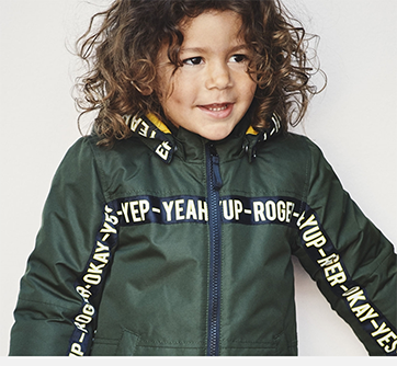 Barn i grøn jakke med tekst, smiler og ser til siden.