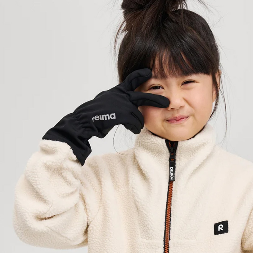 Lille barn med brun hue holder hånden for munden og smiler.