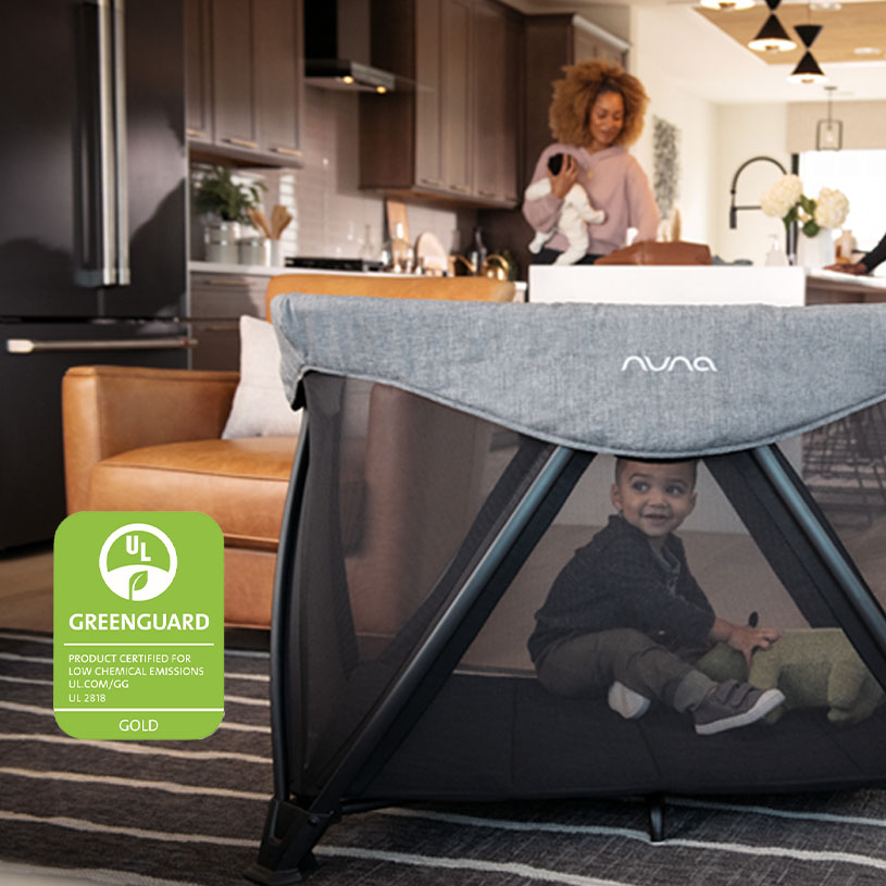 Børneseng i køkken med smilende barn, legetøj og voksen i baggrunden.