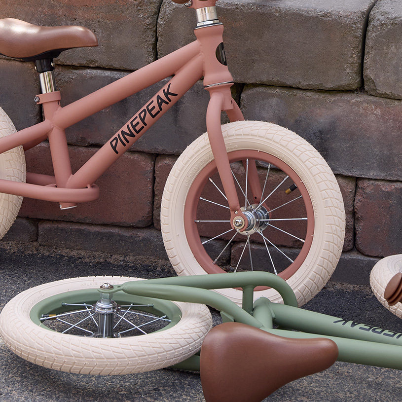 Gul børnecykel med kurv og støttehjul foran puder og væg.