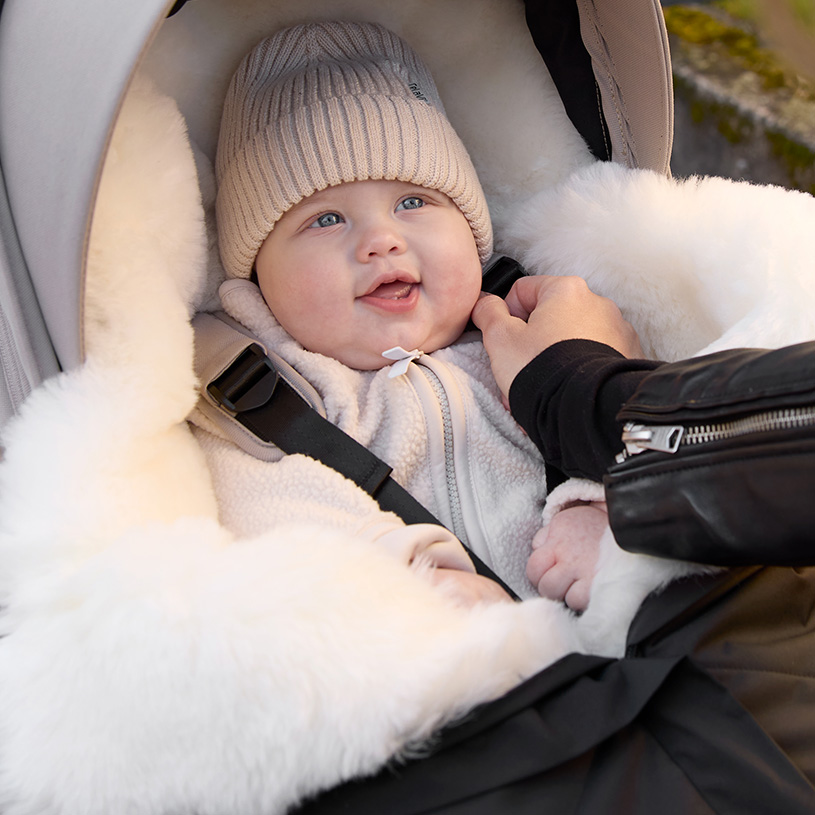 Baby med sut sover i en sort flyverdragt i autostol.