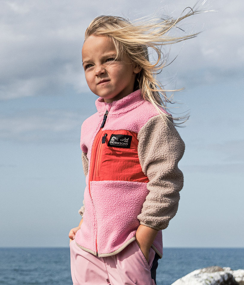 Et barn i en farverig fleecejakke står ved en sø.