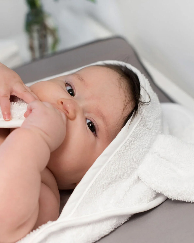 Baby i hvidt håndklæde kigger op og suger på fingrene.