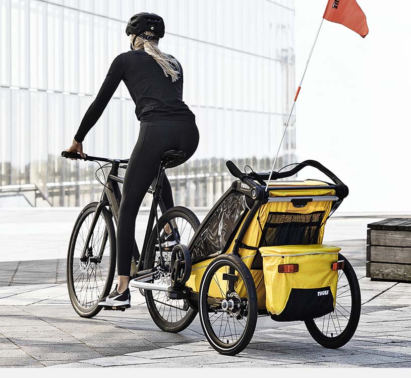 Person cykler med en gul cykelanhænger på fortovet.
