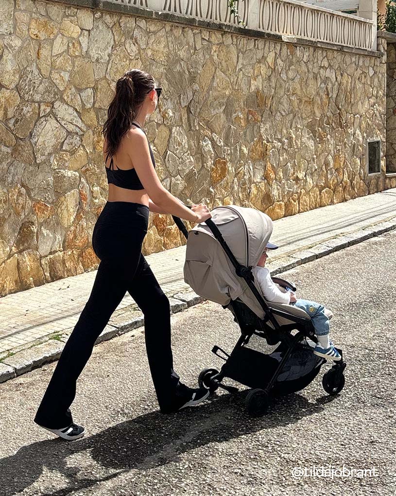 Kvinde skubber klapvogn ved stenvæg.