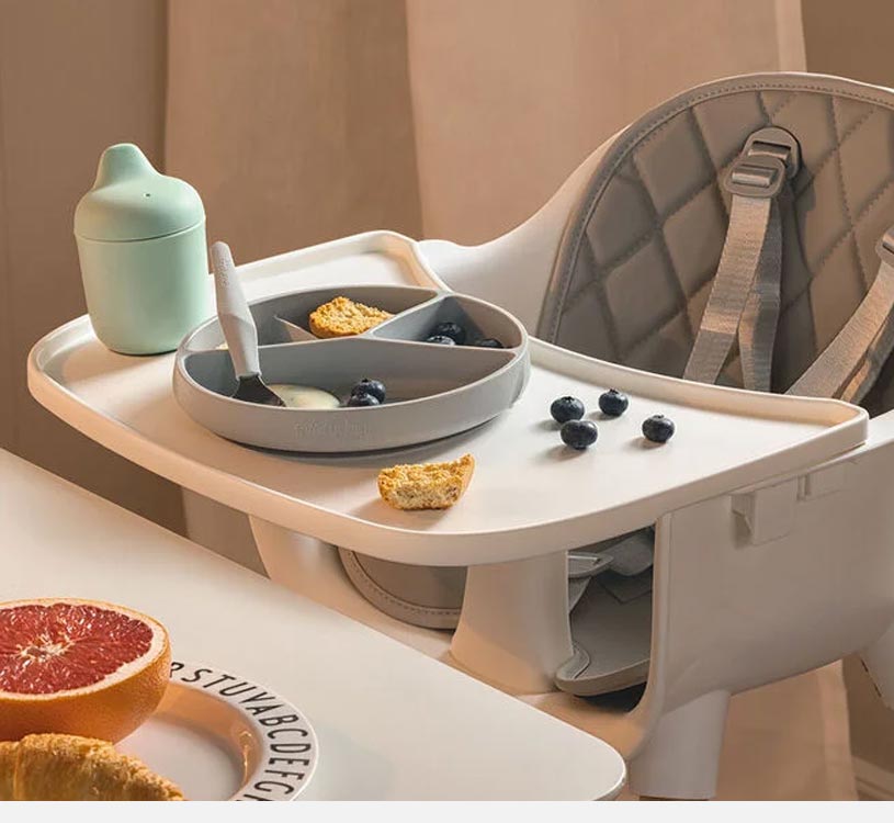 Højstol med bakke, tallerken med mad, bær og tudkop.