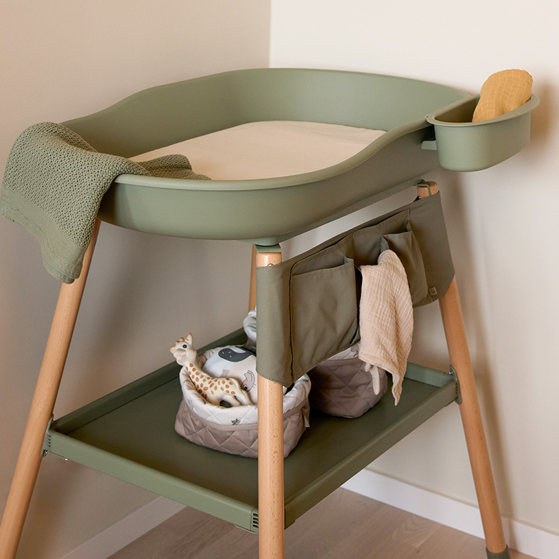 En baby ligger på et puslebord, mens en voksen skifter ble.