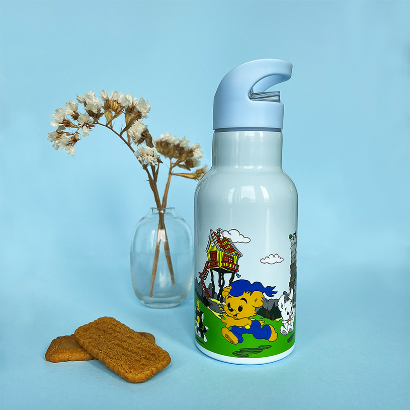 Vandflaske med bjørnemotiv, blomster i vase og kager på blå baggrund.