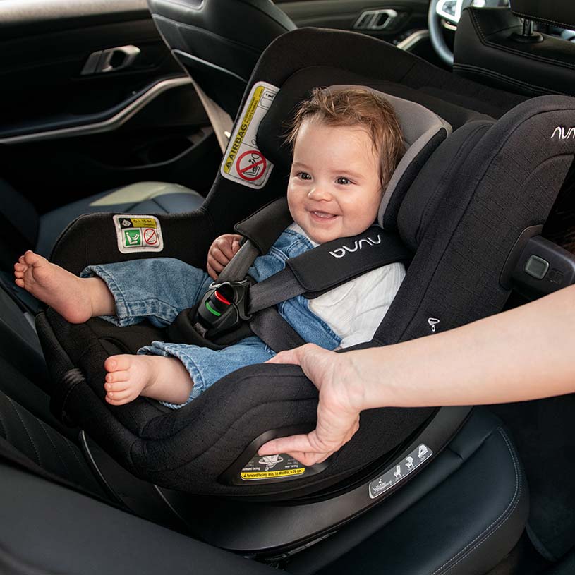 Baby i autostol, smilende og holdt af en voksen.