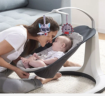 Kvinde smiler til baby i vippestol med legetøj over.