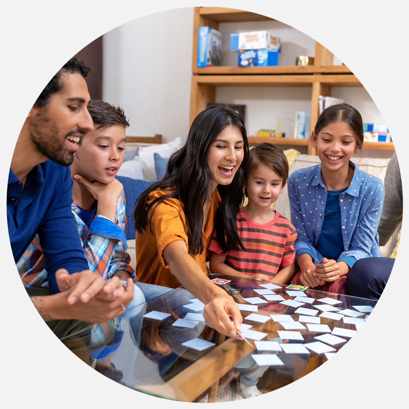 Fem personer spiller kortspil ved et rundt bord i en stue.