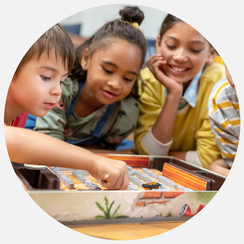 Børn spiller et brætspil og ser koncentrerede ud.