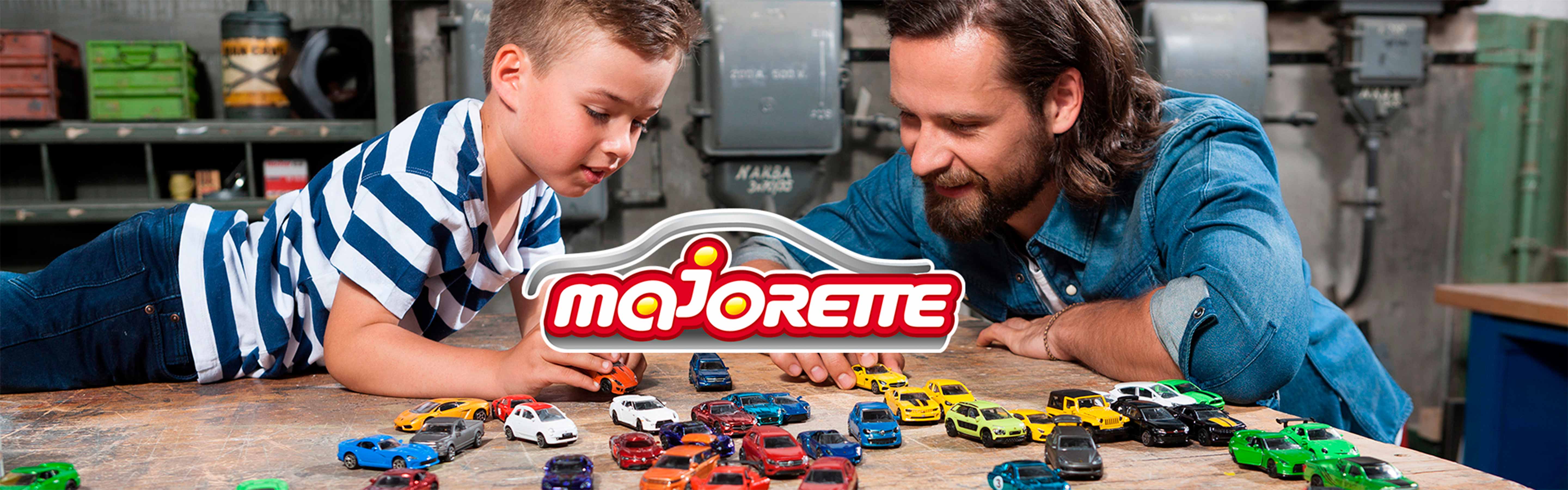 To personer leger med små biler på et bord i et værksted-lignende rum.