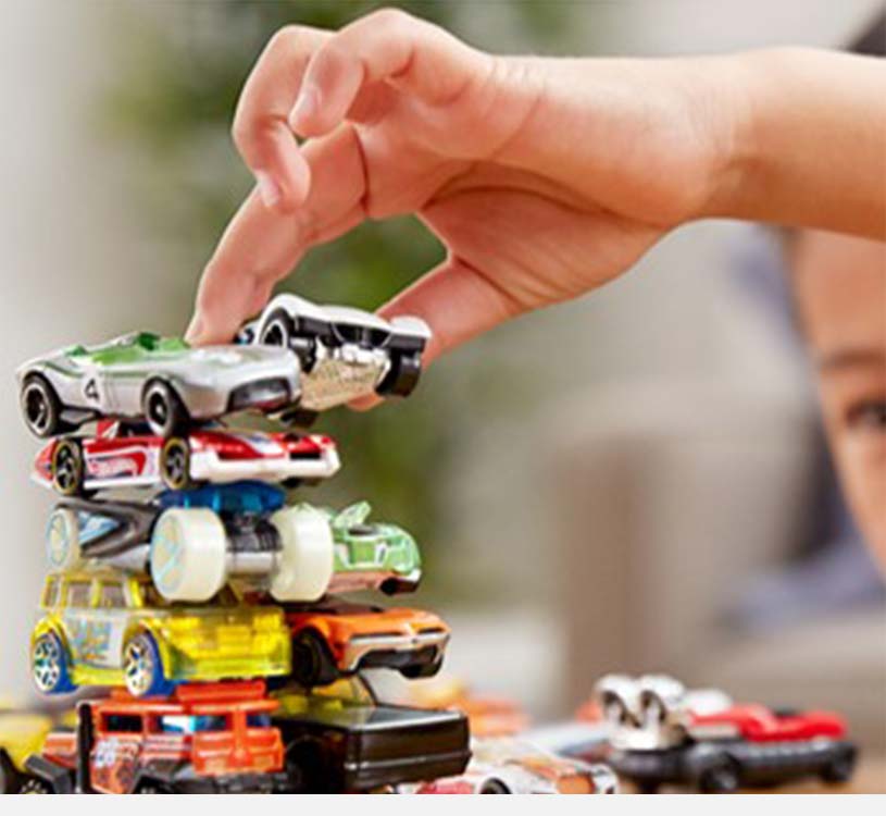 En hånd stabler legetøjsbiler oven på hinanden.
