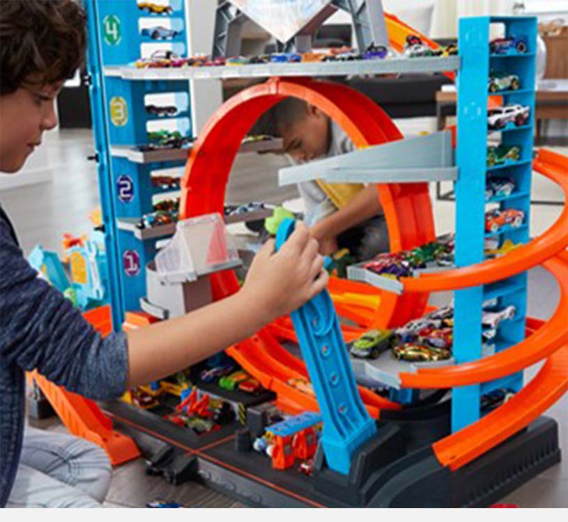 Børn leger med stor legetøjsbilbane med orange ramper.