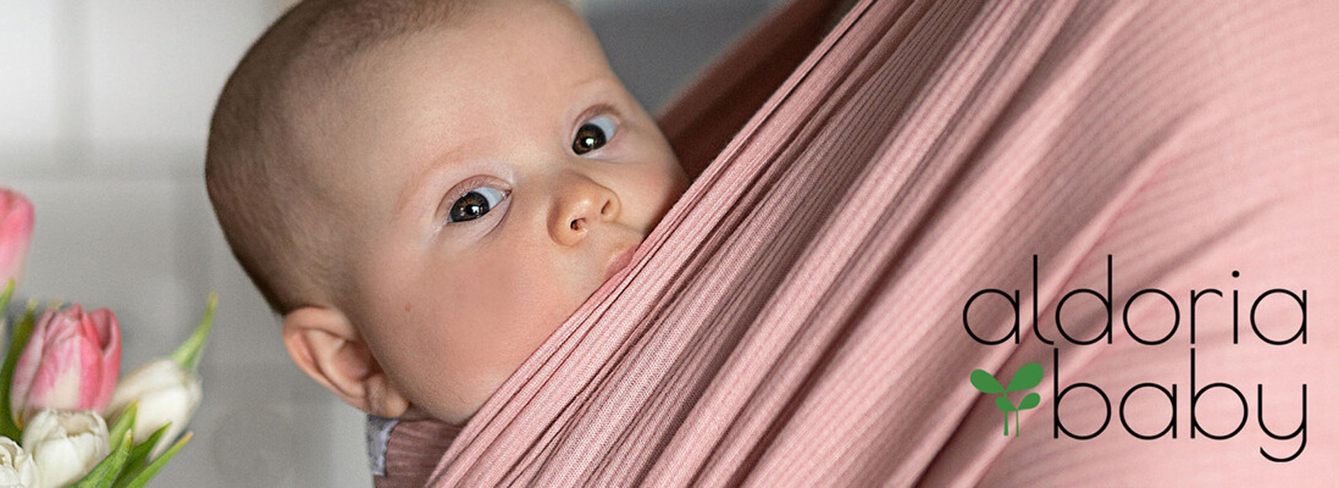 Baby i en lyserød vikle med tulipaner i baggrunden.