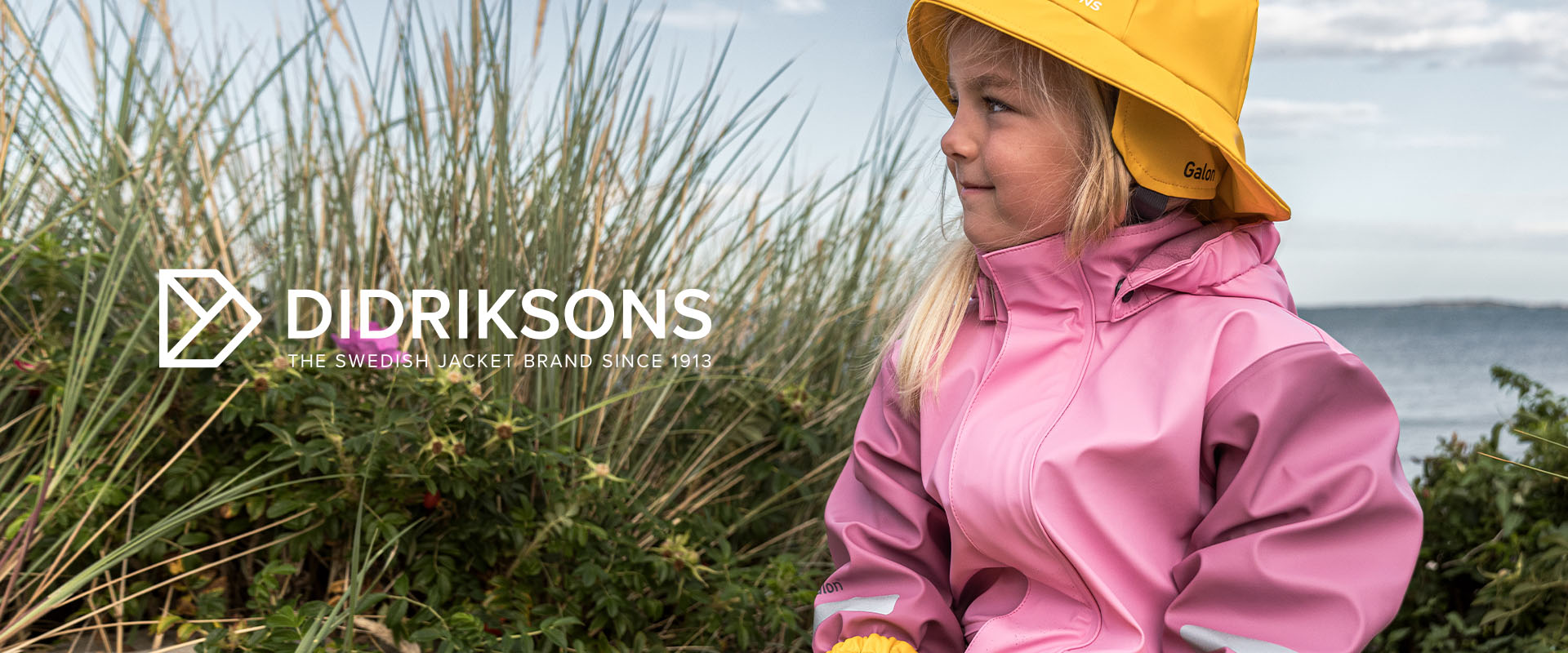 Tre børn på en bro iført farverige jakker ved søen.