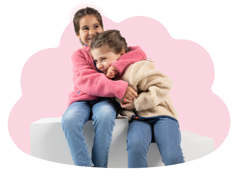 To børn i fleecejakker sidder på en hvid bænk mod lyserød baggrund.