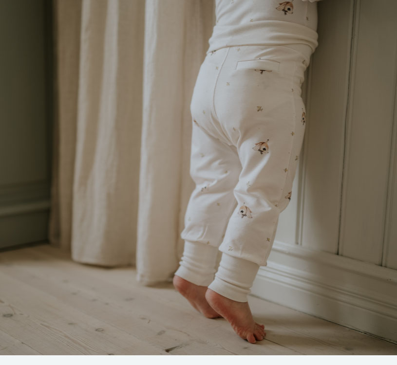 Barn i hvid pyjamas står på tæerne ved gardin.