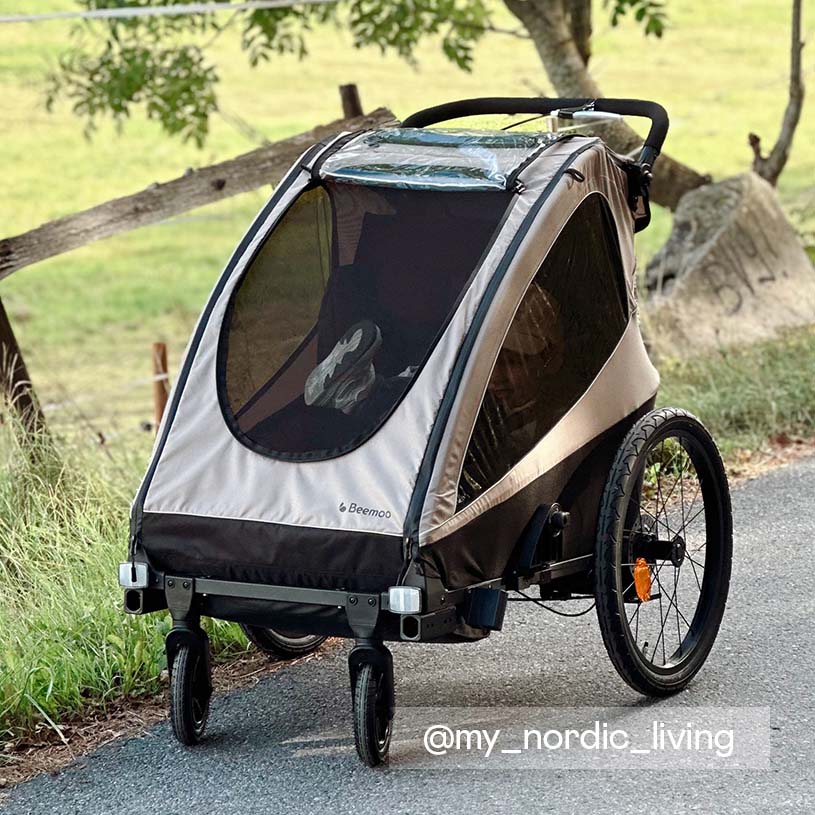 Kvinde og barn holder i hånd og går mod en sort cykeltrailer.