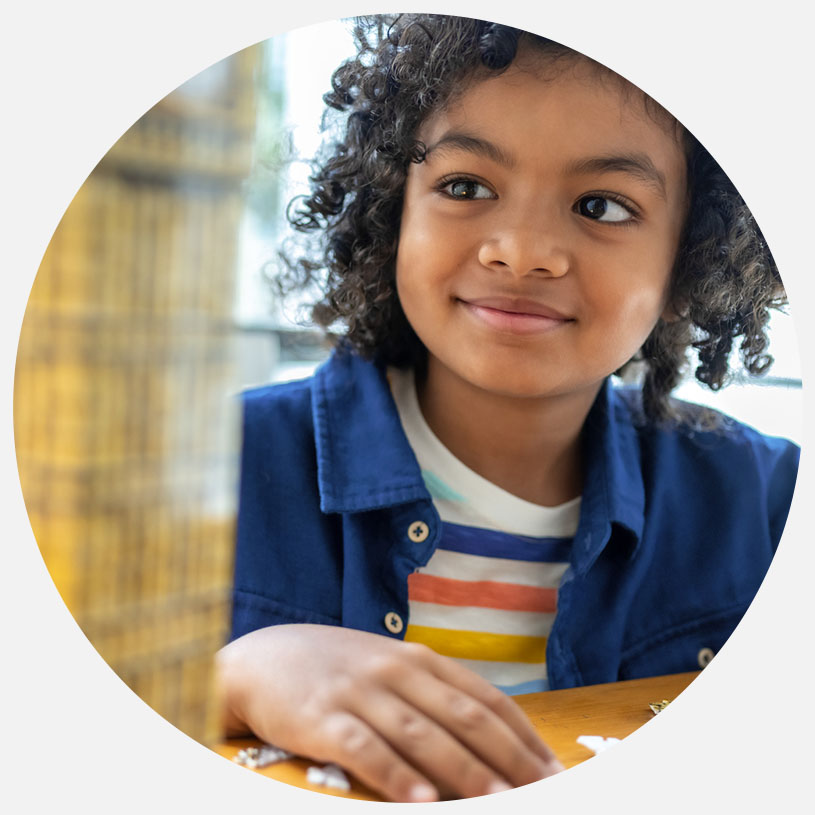 Dreng med krøllet hår smiler indendørs.