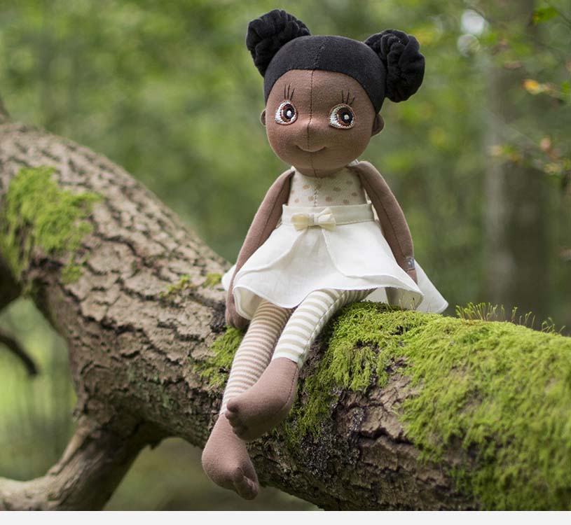 Dukke i hvid kjole på mosdækket træstamme i skoven.