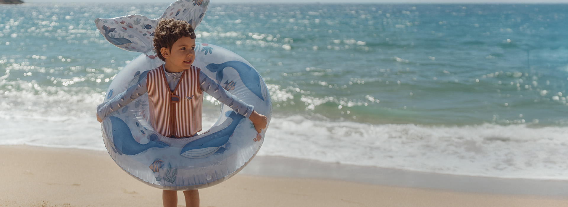 Barn på strand med badering, hav i baggrunden. Tekst: "Nyt for sæsonen".