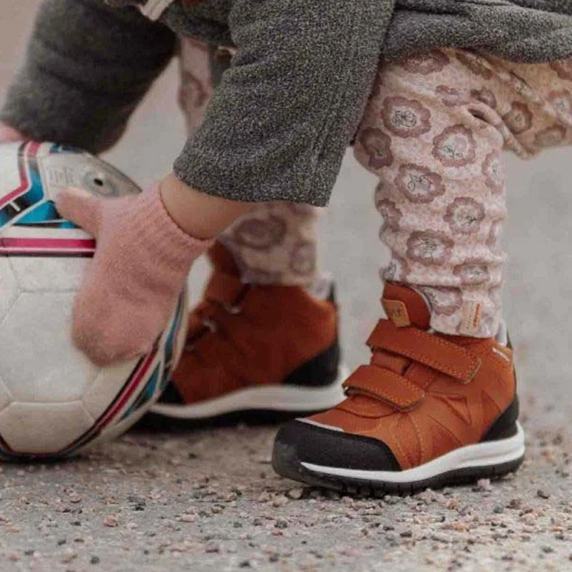 Barn i støvler sparker bold på grus.